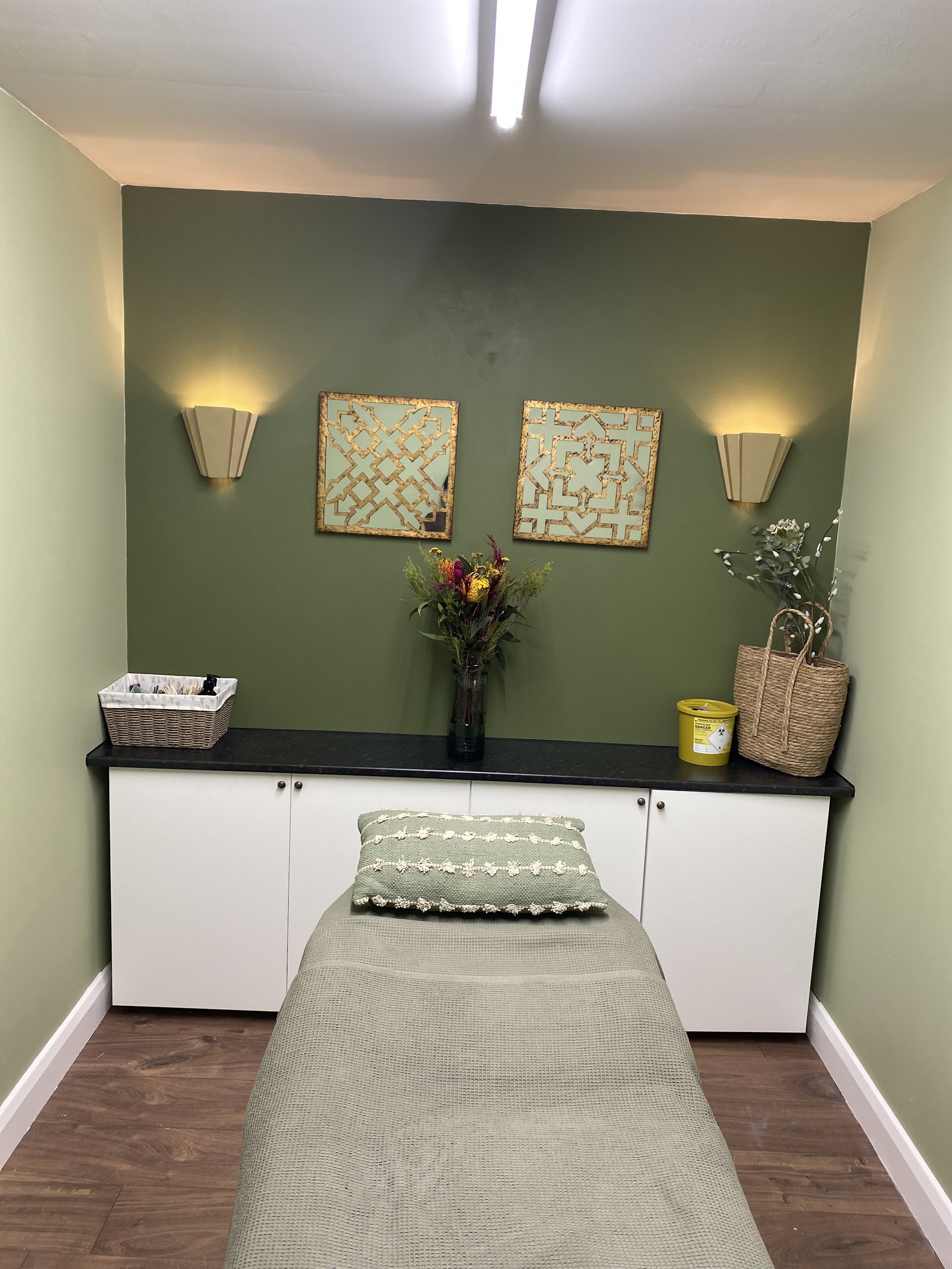Jana's treatment room with a sage green wall, gold framed prints and the treatment couch